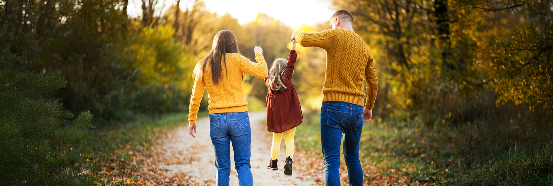 Family walking hand-in-hand through a scenic forest trail during autumn, symbolizing the joy and connection of affordable family vacations in nature.