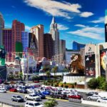 Daytime view of the Las Vegas Strip featuring iconic luxury hotels including MGM Grand and New York-New York, with the replica Statue of Liberty, roller coaster, and vibrant cityscape.