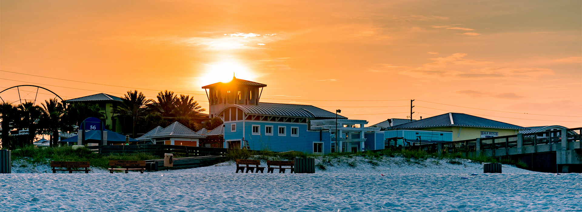 A breathtaking sunset over beachfront properties and hotels in Panama City Beach, with white sand, cozy beach houses, and golden skies creating the perfect vacation vibe.
